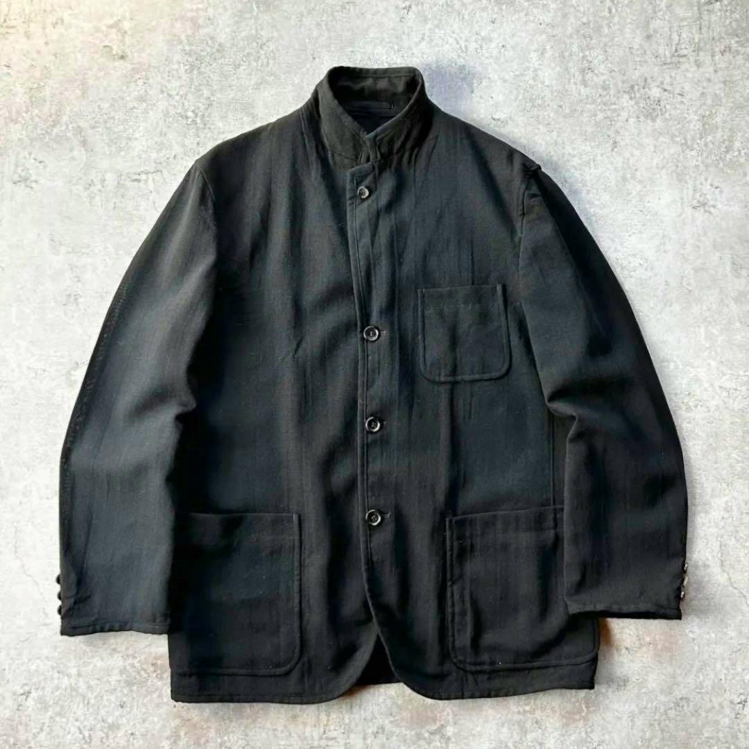 Black men's tailored wool jacket with a stand collar laid flat, showing front buttons and three patch pockets.