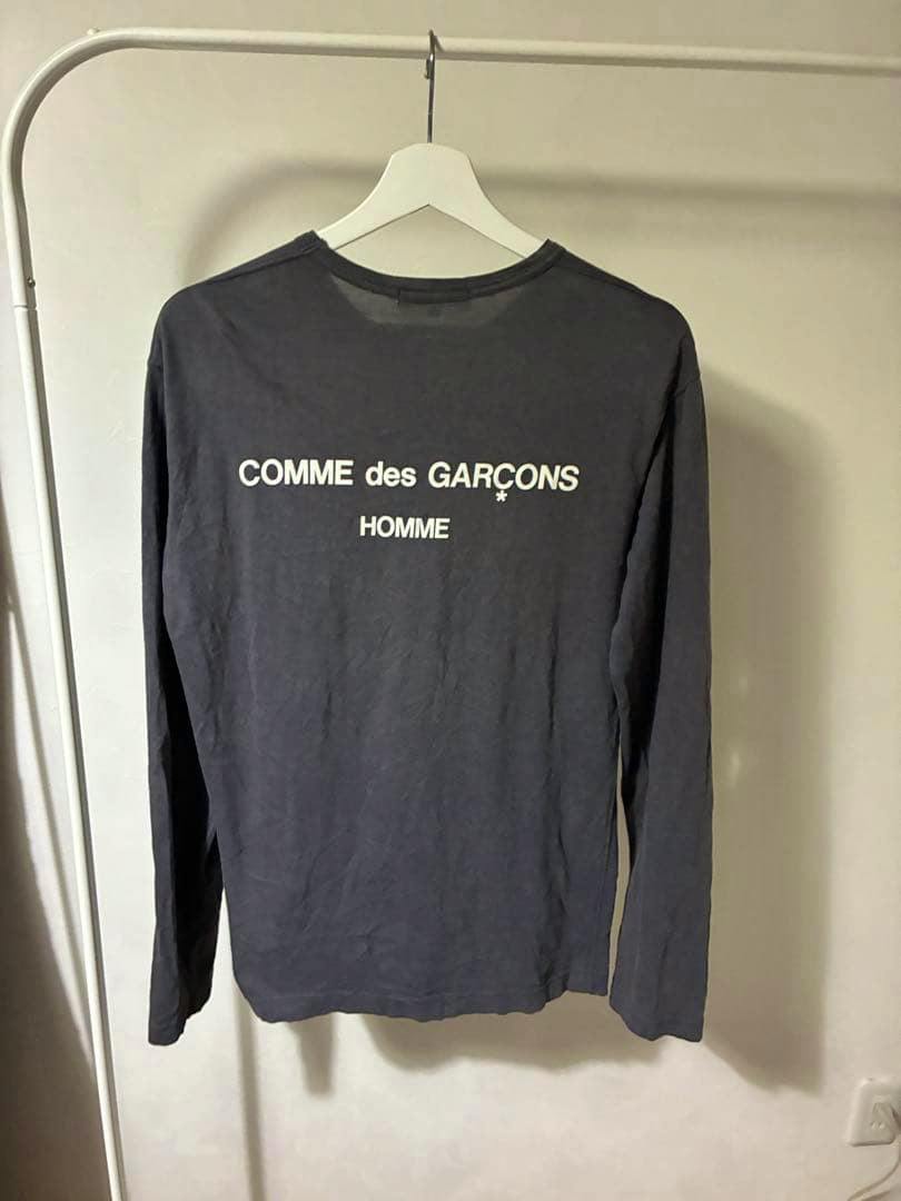 Back view of a men's cotton long-sleeve T-shirt hanging on a white hanger showing a white "COMME des GARCONS HOMME" logo.