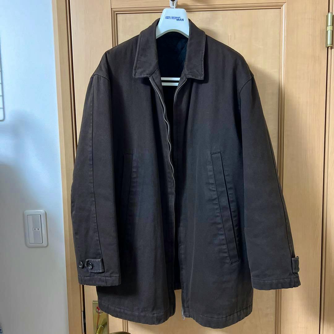 Front view of a dark men's cotton woven jacket hanging on a hanger, showing the collar, zipper, and front pockets.