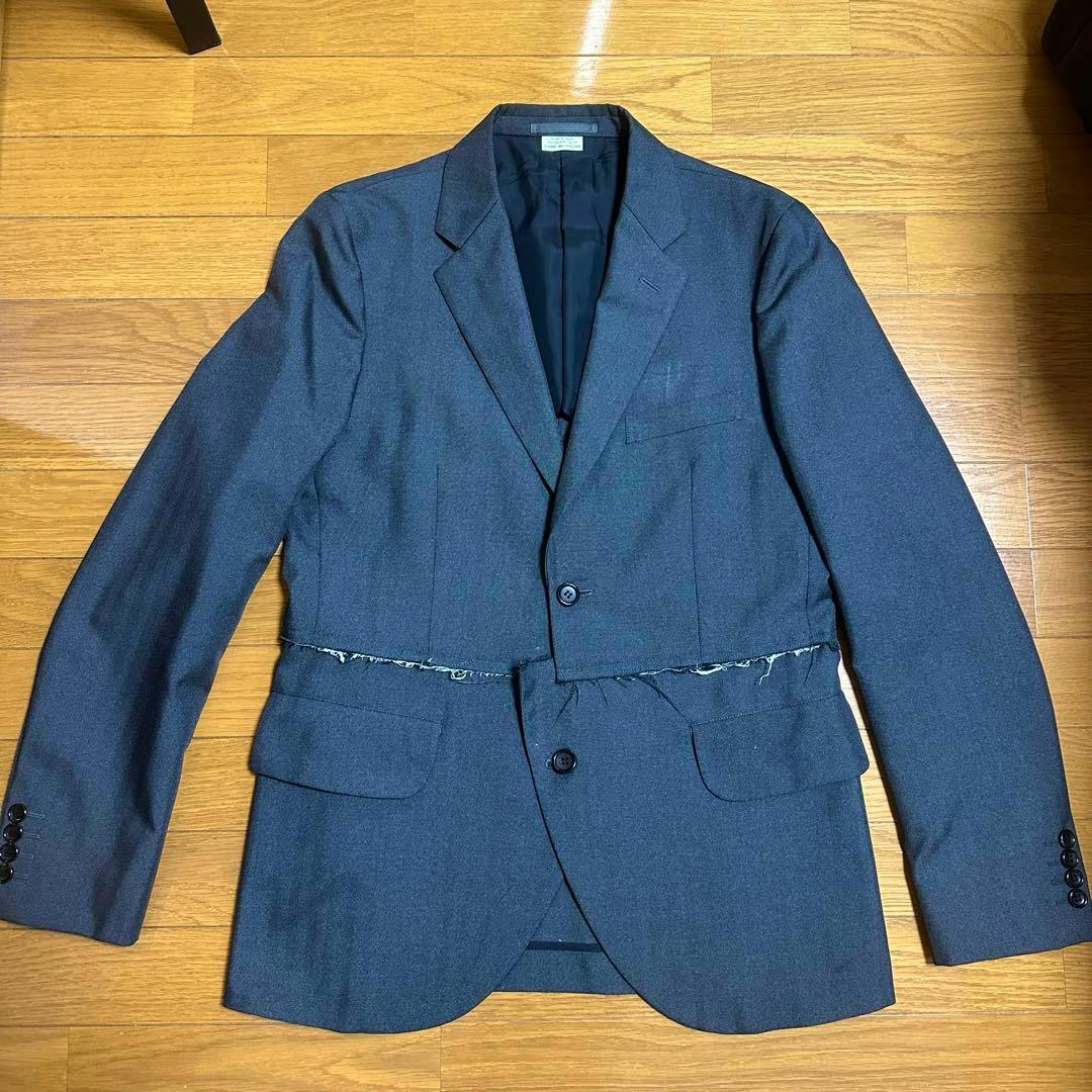 COMME des GARÇONS HOMME DEUX tailored men's jacket laid flat on a wooden floor showing the front with a frayed seam at the waist.
