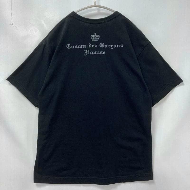Black Comme des Garçons Homme T-shirt hanging on a hanger showing the back with an Old English style back logo print and a crown above the text.