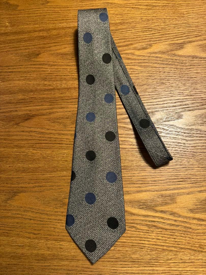 COMME des GARCONS HOMME dot-pattern silk necktie laid flat on a wooden tabletop.