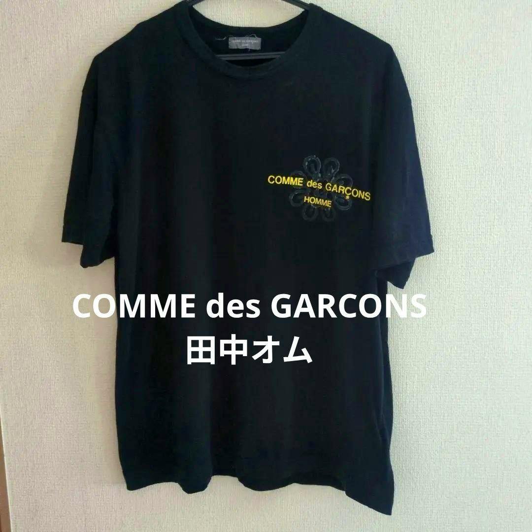 Front of a black COMME des GARÇONS HOMME men's cotton T-shirt hanging on a hanger showing the chest logo.