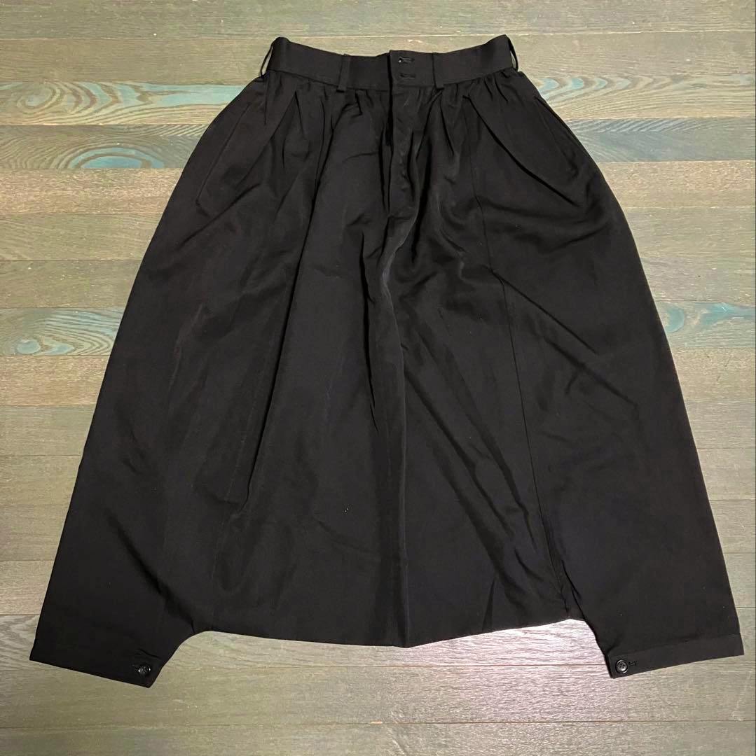 Black sarouel-style women's polyester pants laid flat on a wooden floor, showing the front view.