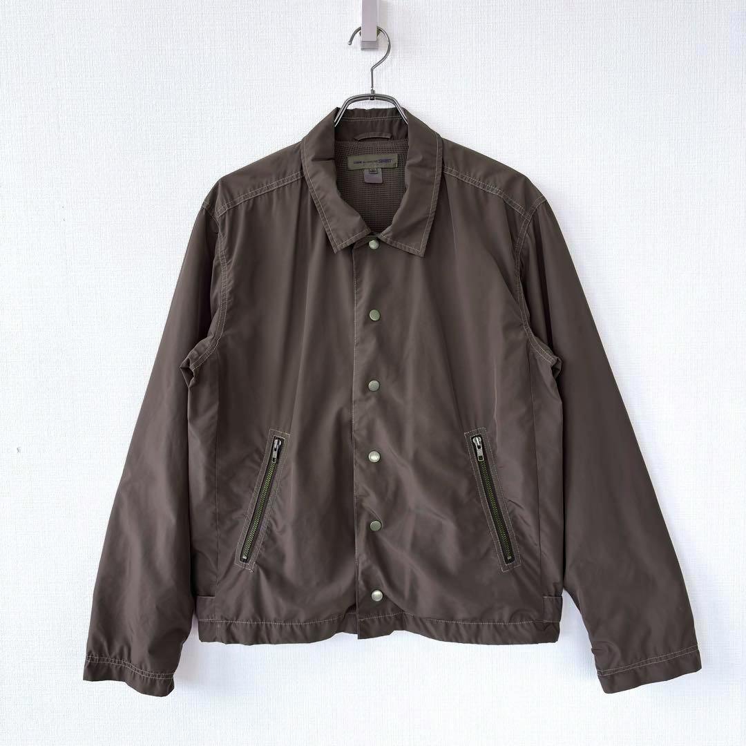 Front view of the 2007SS COMME des GARCONS SHIRT brown polyester blouson jacket hanging on a hanger, showing snap buttons and zip pockets.