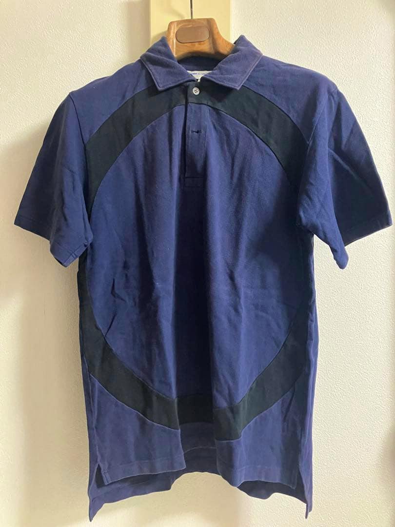 Front view of a navy and black COMME des GARCONS SHIRT short-sleeve polo hanging on a wooden hanger.