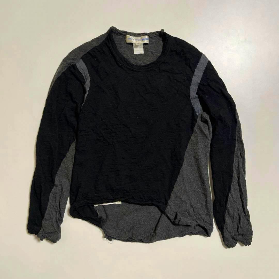 Front view of a two-tone black and gray COMME des GARÇONS sweater laid flat on a light background showing the neckline label.