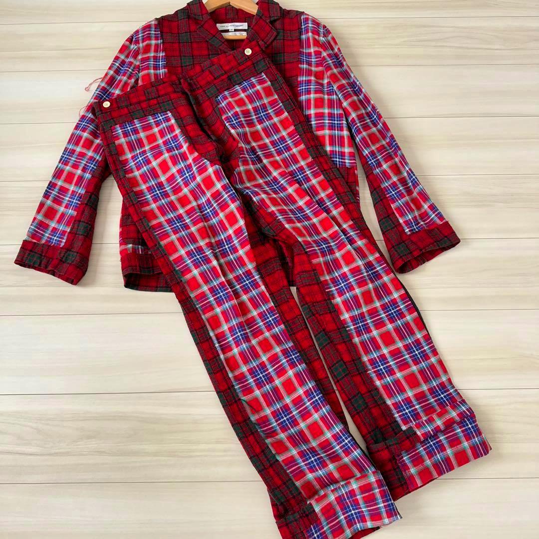 Red Comme des Garçons SHIRT patchwork jacket and matching pants laid flat on a light wood floor.