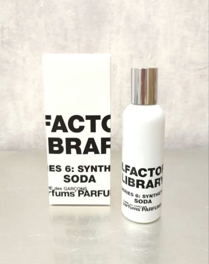 White 50ml Comme des Garçons 'Series 6: Synthetic Soda' perfume bottle with silver cap beside its white box.