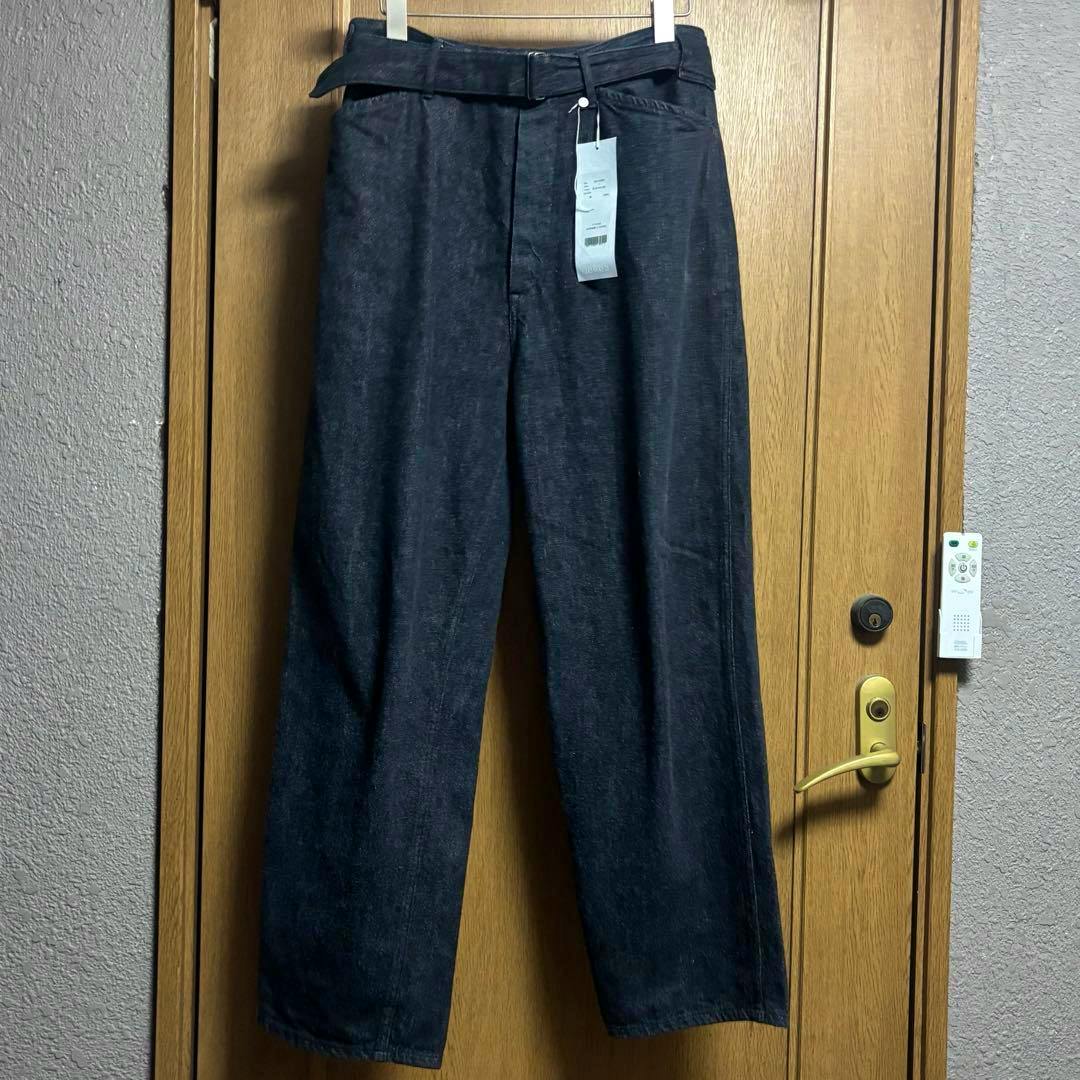 Front view of black belted men's cotton pants hanging on a hanger with tags attached.