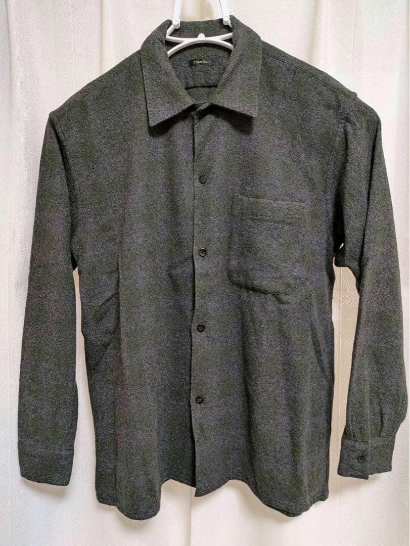 Front view of a gray textured COMOLI open-collar button-up shirt with a chest pocket hanging on a hanger.