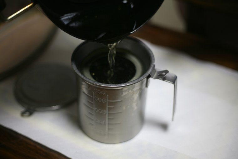 Stainless steel tea strainer set in a small measuring cup while tea is being poured into it.