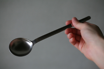 A metal spoon held in a hand against a plain gray background.