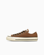 Side view of a brown canvas low-top sneaker with a white rubber sole and black stripe.