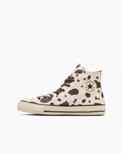 Side view of an ALL STAR AGED COWSPOT HI high-top tennis shoe with a cream upper and brown cow-spot pattern on a white background.