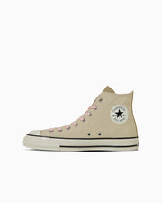 Beige high-top canvas sneaker shown in side view on a white background, displaying the rubber sole and circular ankle patch.