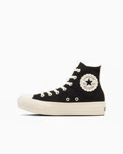 Side view of a black high-top canvas sneaker with a white sole and a floral-cut ankle patch.