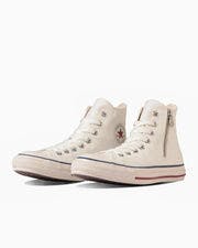 A pair of light-colored high-top canvas sneakers with a side zipper and star logo on a white background.