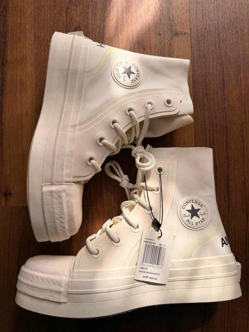 Off-white Converse All Star x Ambush high-top sneakers shown side view on a wooden floor with the Converse patch and a hanging price tag visible.