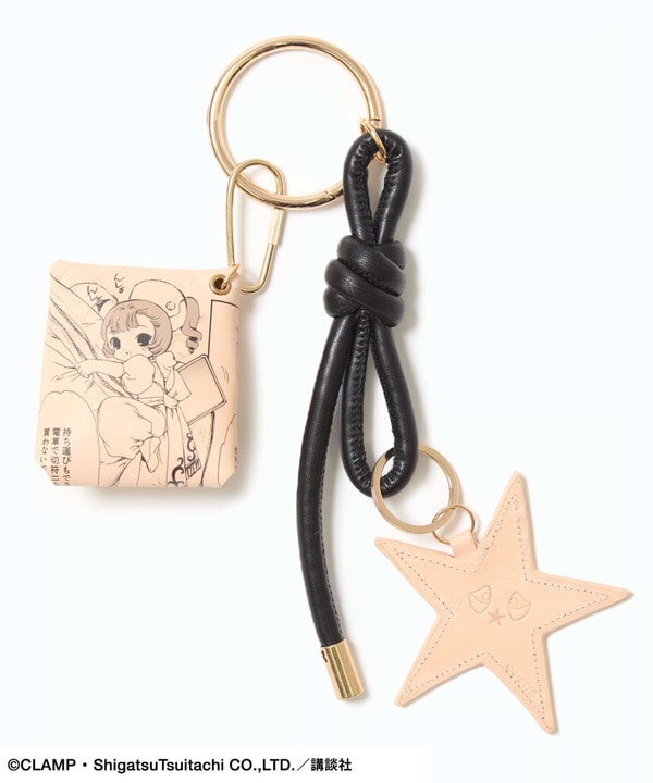 Cow-leather keychain pouch charm showing a printed square pouch, knotted black leather strap, and a pale star-shaped leather charm on a gold ring.