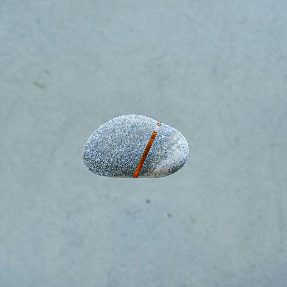 A smooth gray stone with a narrow amber-colored glass inlay set across its surface on a plain gray background.