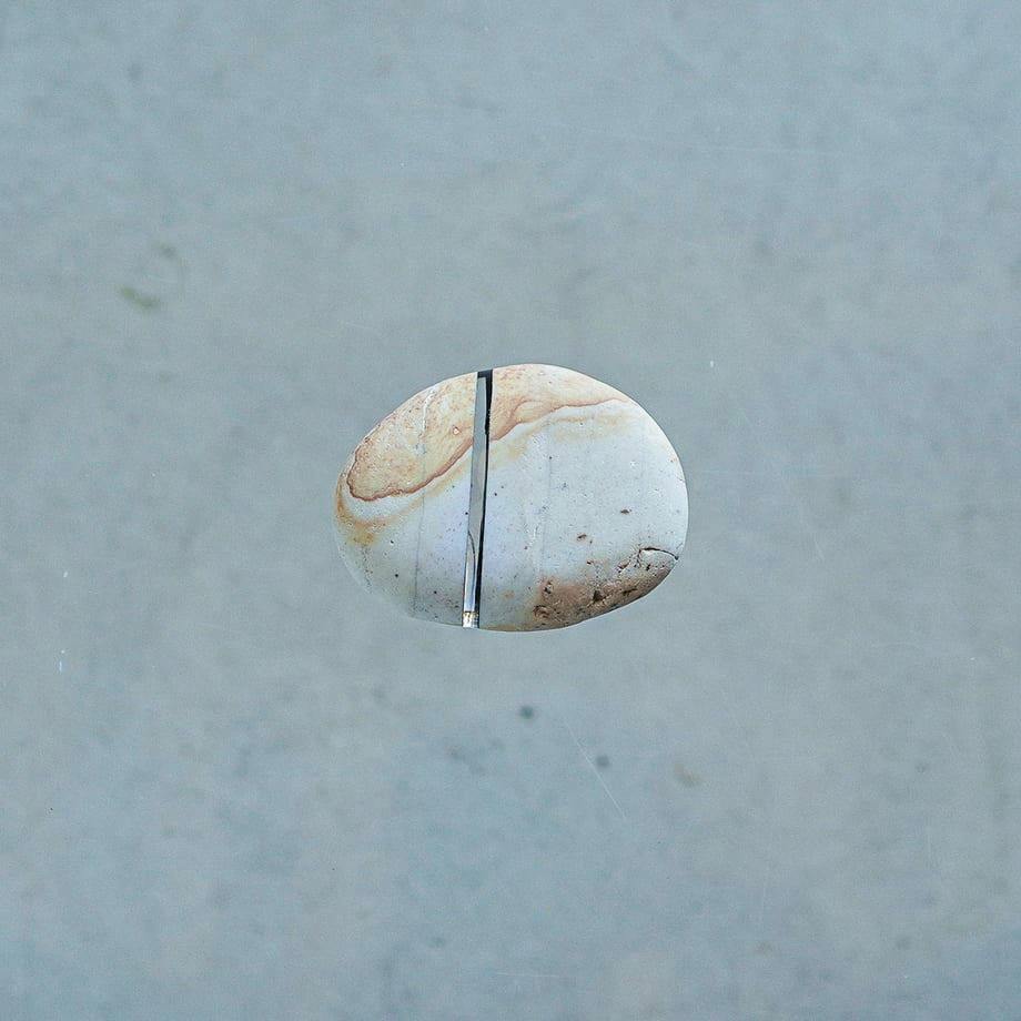 A rounded light-colored stone with a thin vertical glass inlay centered against a plain gray background.