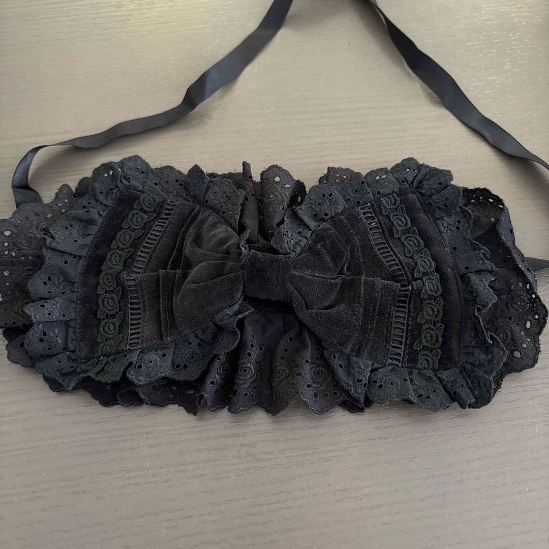 Black velvet headband with a central velvet bow, eyelet-lace ruffles, and long tying ribbons laid flat.