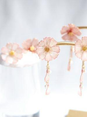 Close-up of pink flower-shaped earrings with small dangling beads displayed on a stand.