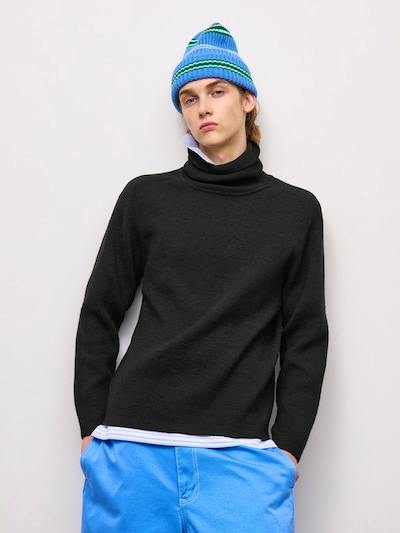 Model wearing a black long-sleeve turtleneck sweater layered over a white shirt and paired with blue pants.