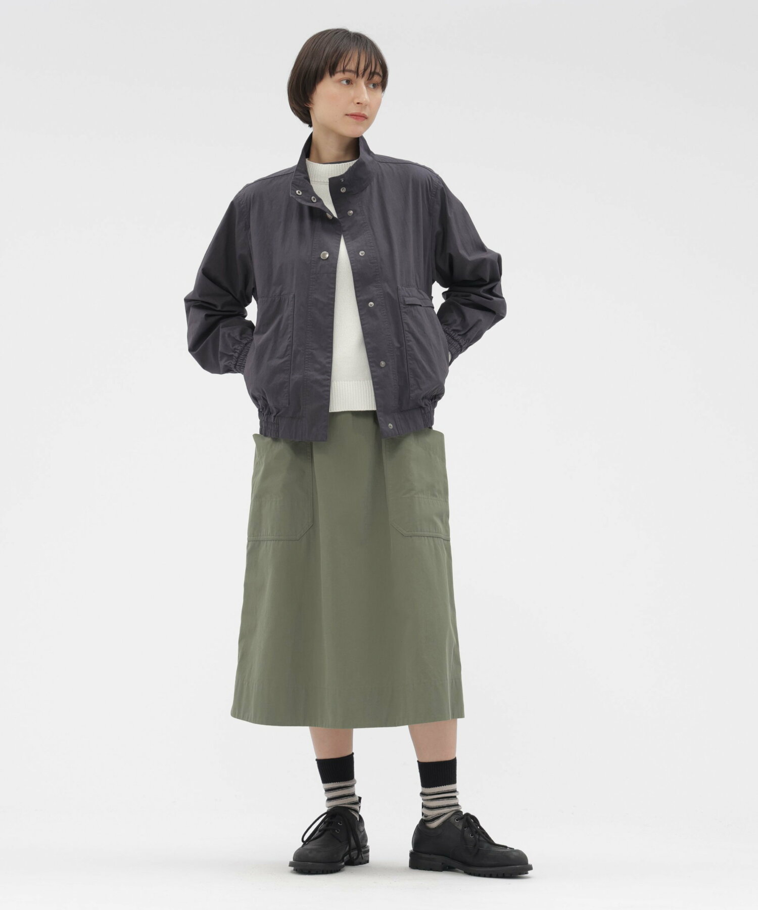 Model wearing an olive-green cotton skirt with visible front patch pockets, shown with a jacket.