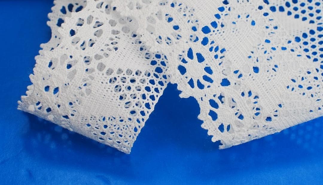 Close-up of off-white cotton lace (45mm width) with a floral crochet pattern on a blue background.
