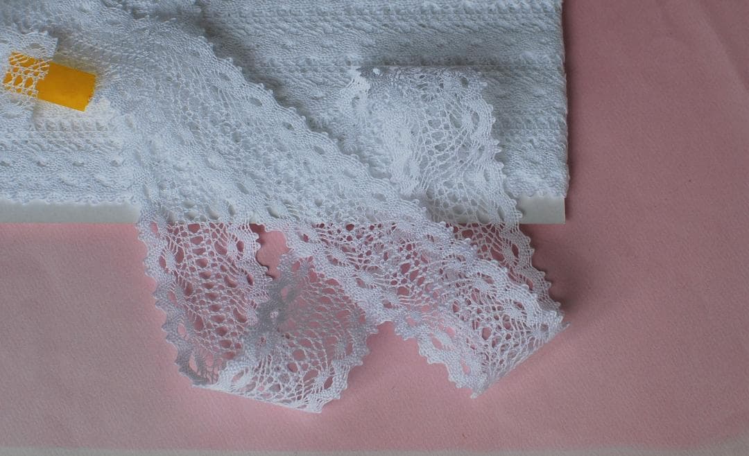 White cotton lace trim (33mm width) rolled on a card on a pink background.