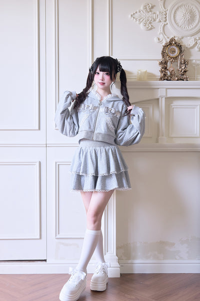 Model wearing the gray cotton race jersey sweater paired with a matching skirt, standing against a decorative wall.