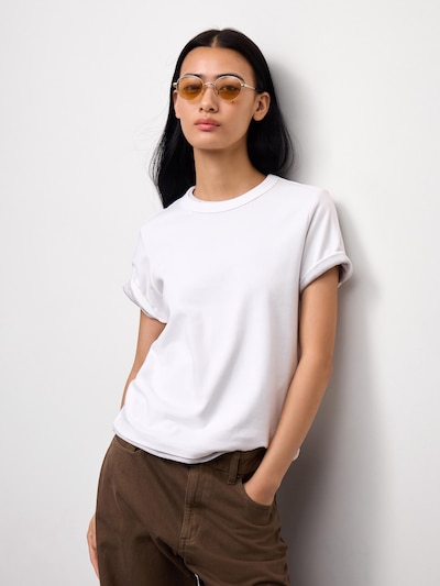 White men's cotton crew-neck T-shirt worn by a model, shown from the waist up leaning against a wall.