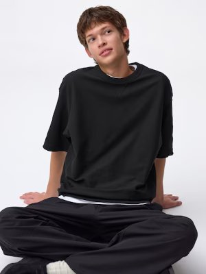 A seated model wearing a black mid-length-sleeve cotton T-shirt over a white undershirt.