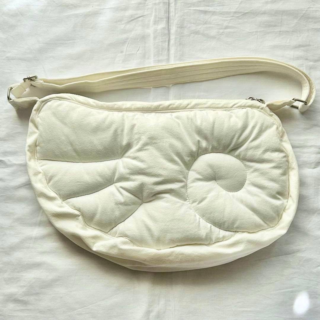 White wing-shaped shoulder bag with quilted padded front and adjustable strap laid flat on a white background.