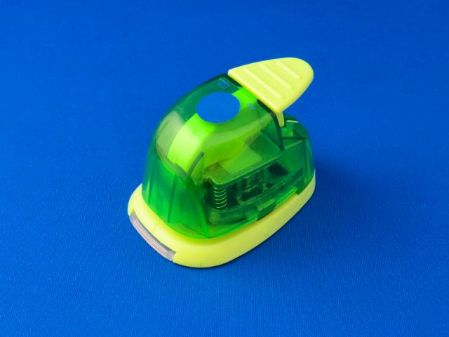 Green and yellow craft hole punch on a blue background.