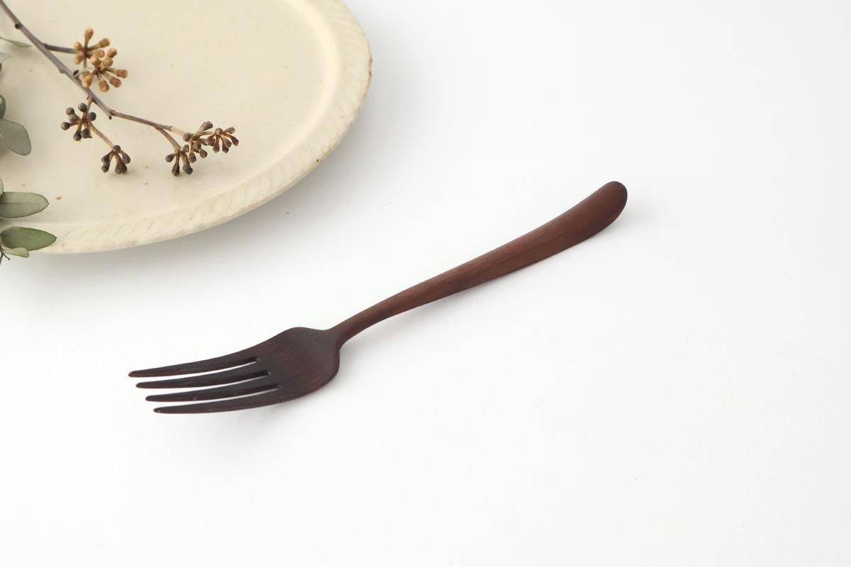 Dark metal pasta fork on a white surface next to a ceramic plate and dried sprigs.