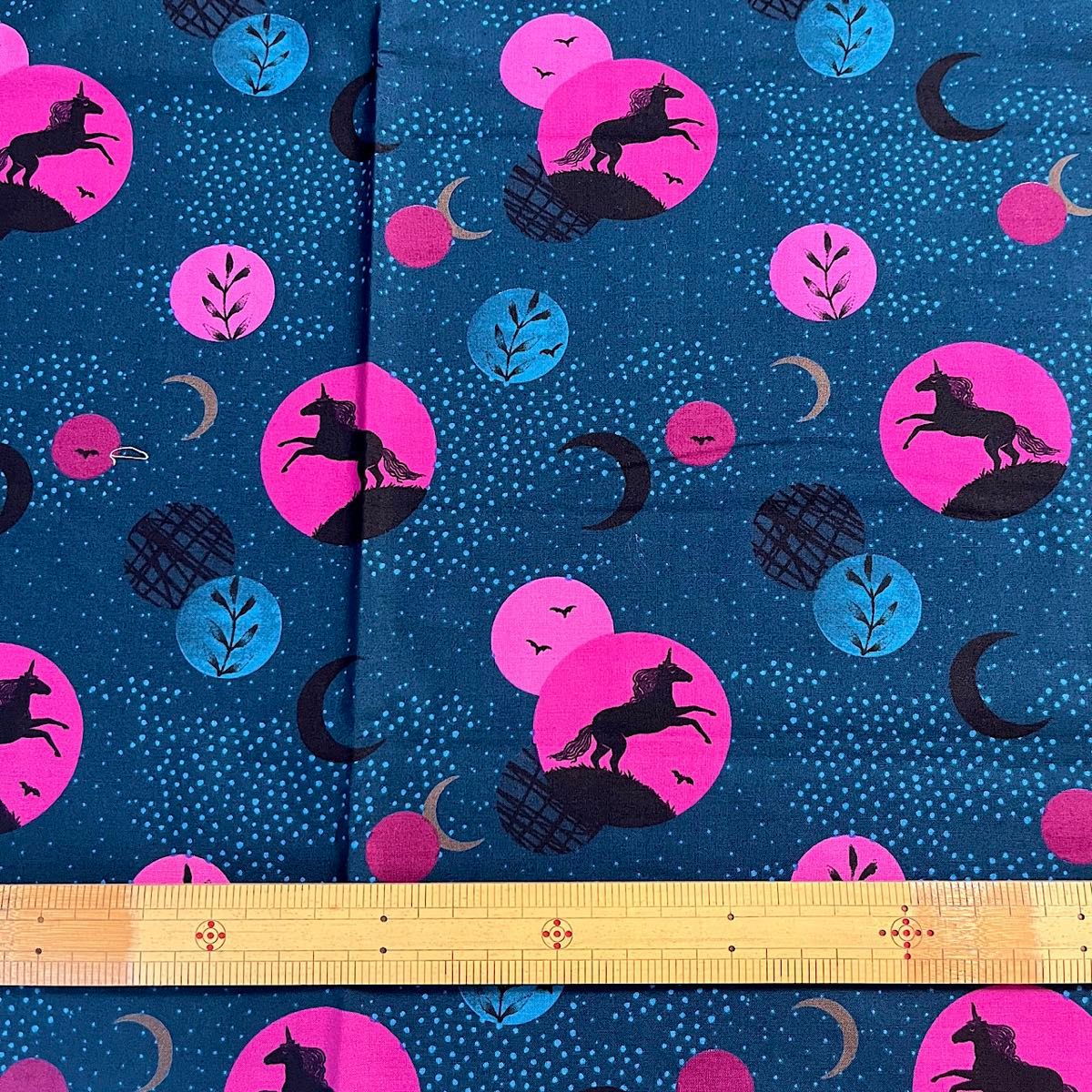 Dark teal cotton fabric with pink and blue circular motifs and black horse/unicorn silhouettes, with a ruler at the bottom for scale.