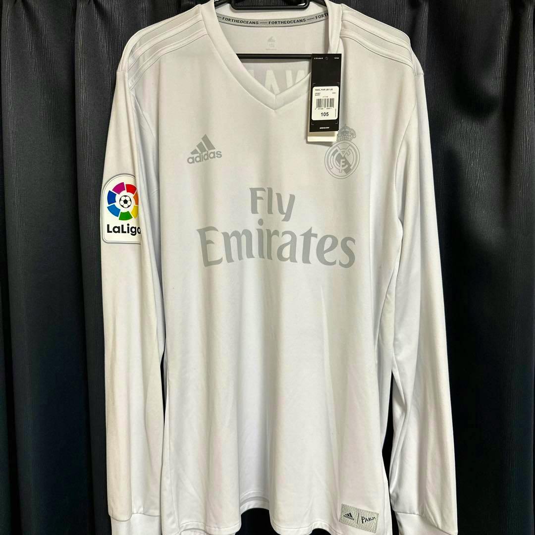 Front view of a long-sleeve Real Madrid polyester jersey showing the Fly Emirates sponsor, club crest, LaLiga sleeve patch, and attached price tag.
