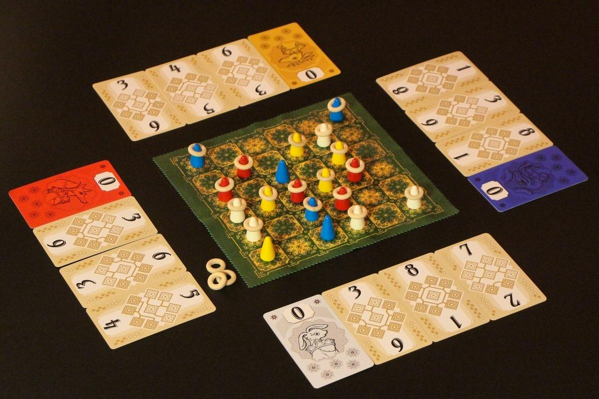 Photograph of the card game setup for 木々の冠 showing the central patterned board with colored cone and pawn pieces and the surrounding numbered cards.