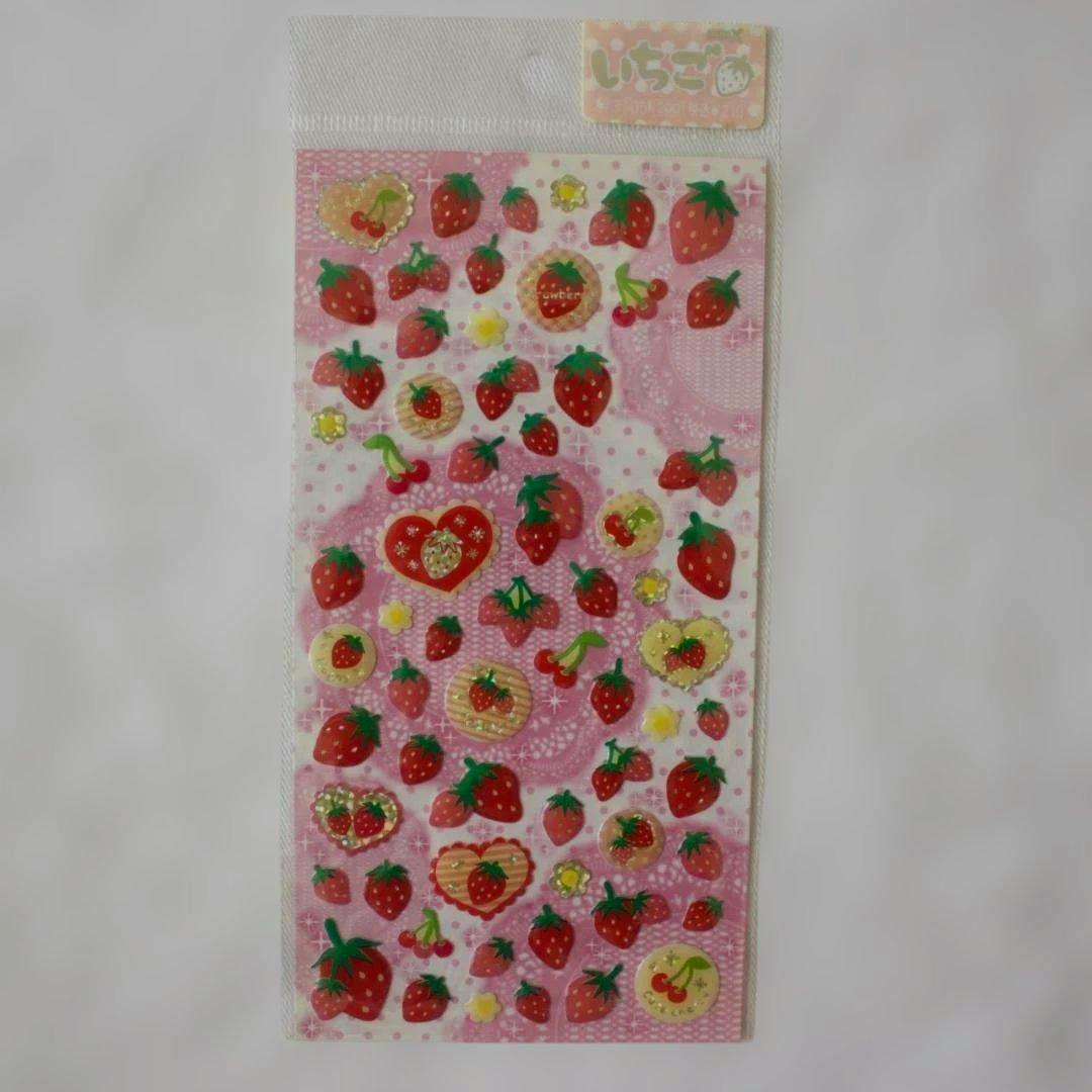 A sheet of paper stickers showing many small strawberry designs on a pink patterned background.