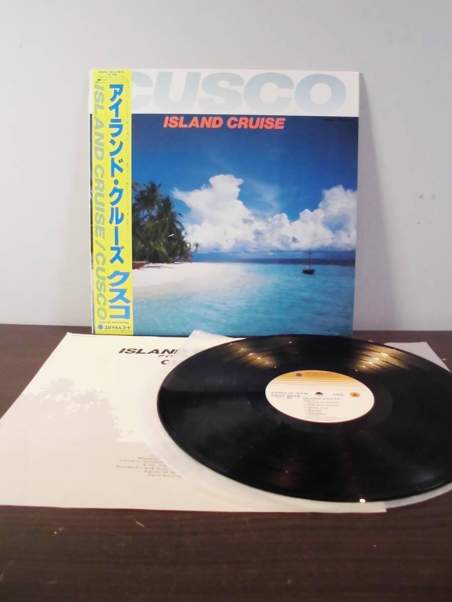 Vinyl record and its album cover for CUSCO "Island Cruise" with a Japanese obi strip displayed on a table.