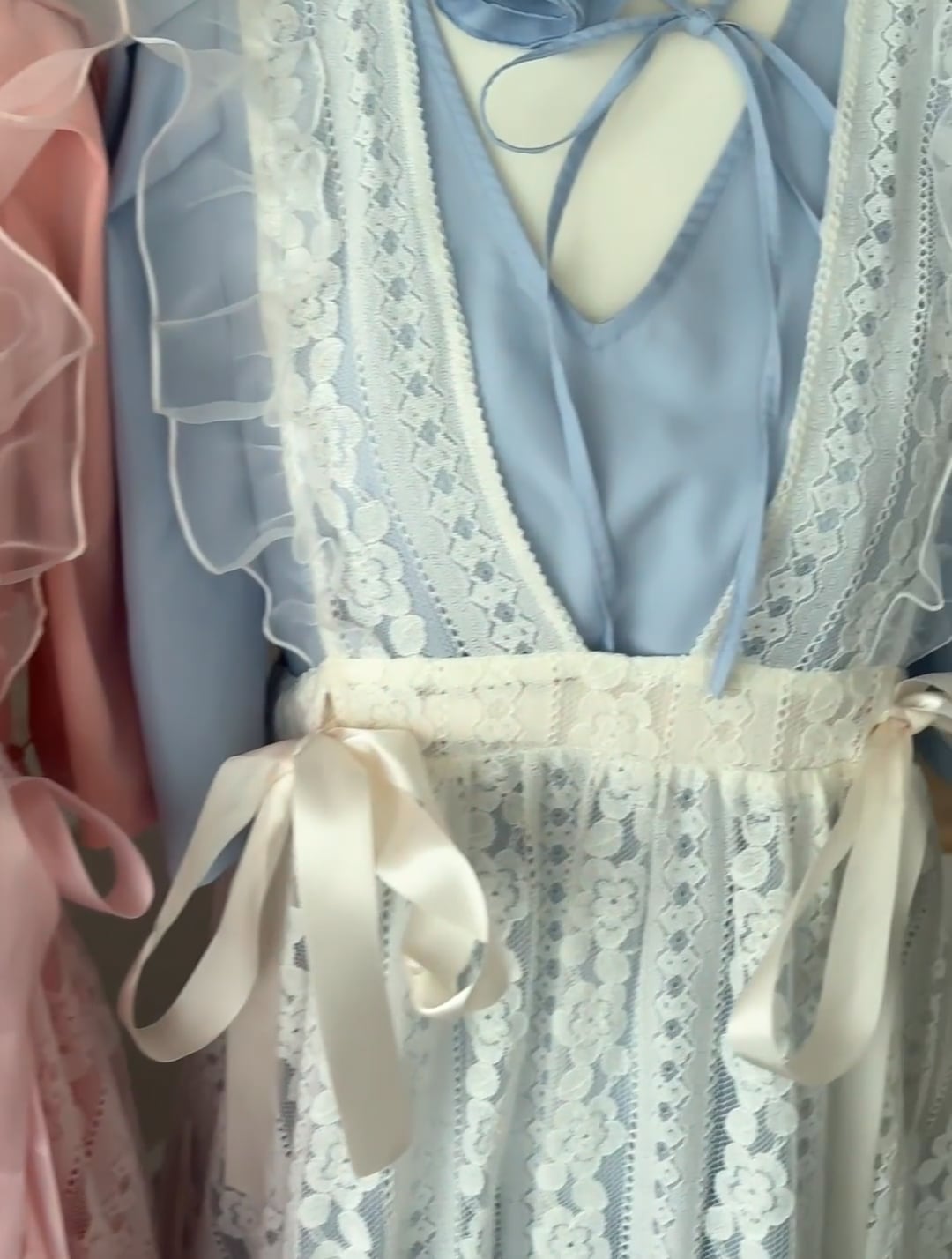 Close-up of a lace ribbon apron dress showing lace overlay, satin ribbon ties, and a blue underdress.