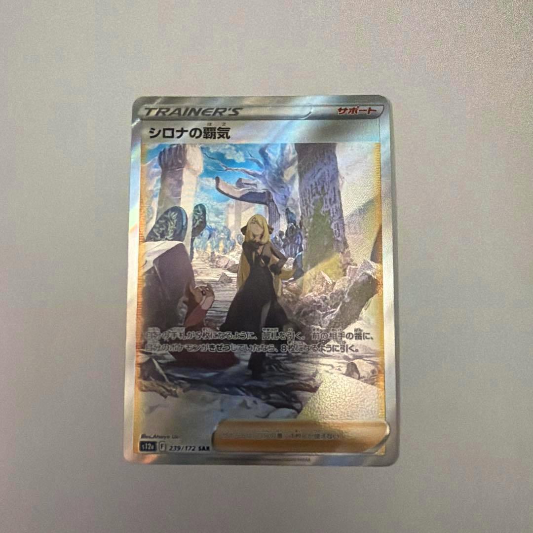 Front photograph of the holographic trading card “シロナの覇気” (trainer card) on a plain surface.