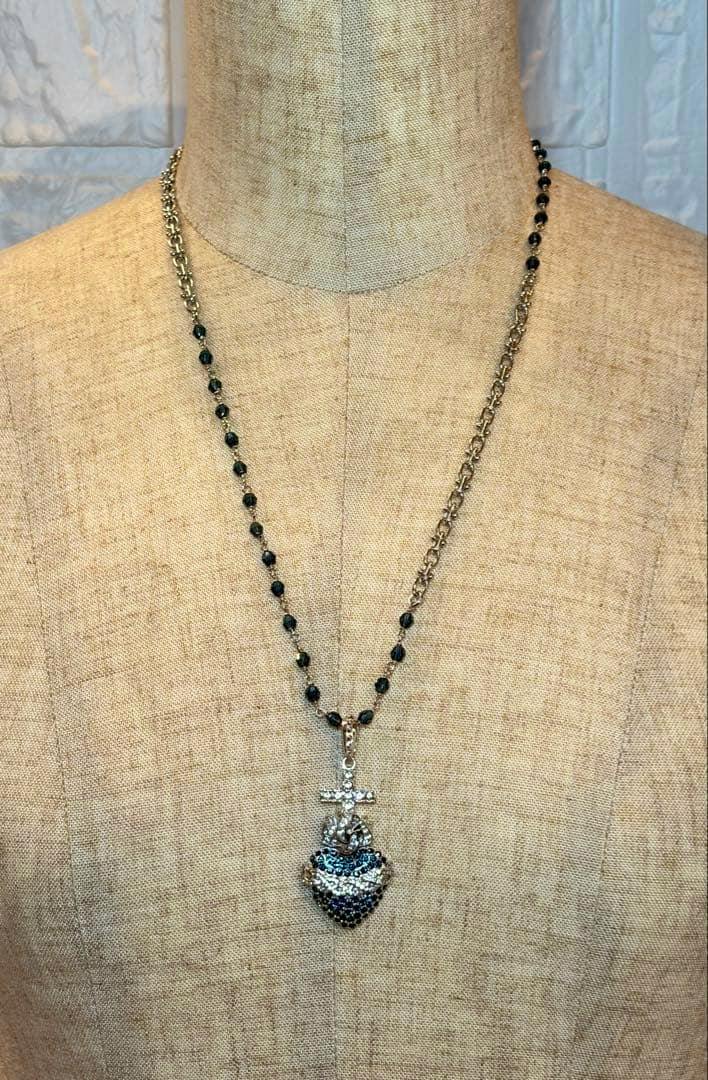 Long Dolce & Gabbana necklace on a mannequin, with a beaded chain and a cross-and-heart pendant set with blue and clear stones.