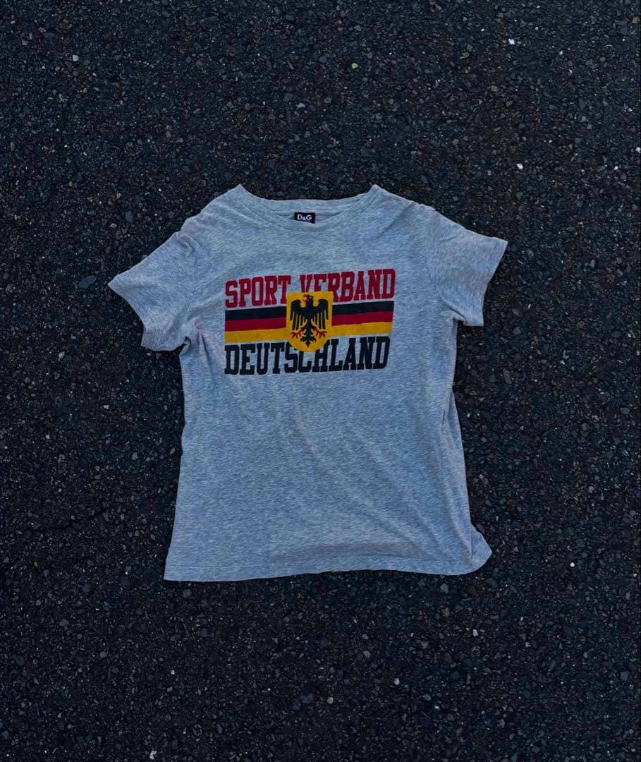 Grey men's D&G Sport T-shirt laid flat showing the front with 'SPORT VERBAND DEUTSCHLAND' text and a German crest print.