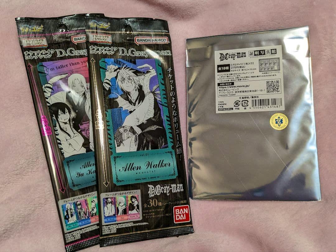 Photo of two D.Gray-man ticket-like collection blind-pack wrappers and one silver foil sealed pack on a pink fabric background.