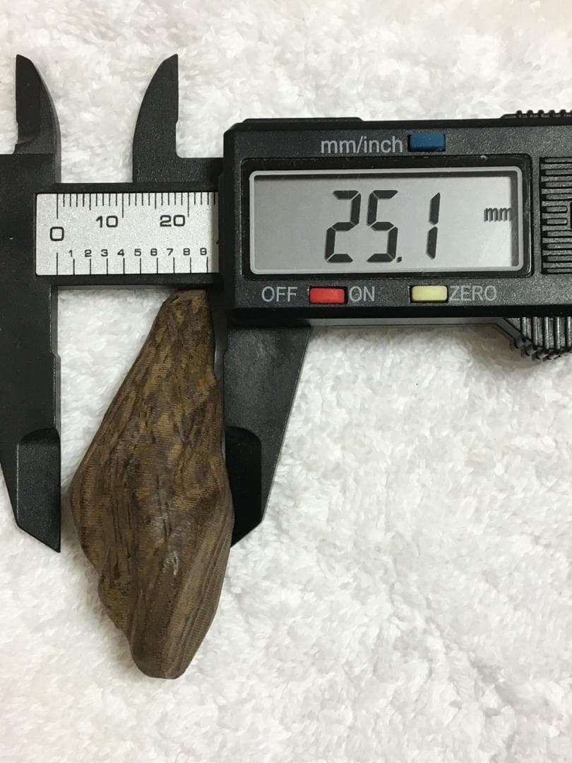 Digital calipers measure a small piece of agarwood incense/ornament showing a 25.1 mm reading.