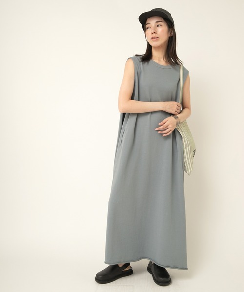 Model wearing a long sleeveless women's cotton tuck-design dress in gray, styled with a cap and tote bag.
